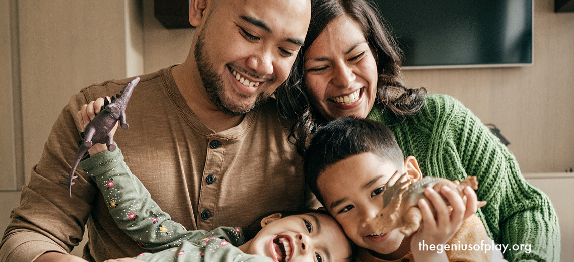 Latin American parents, son and daughter laughing and playing together with dinosaur figures