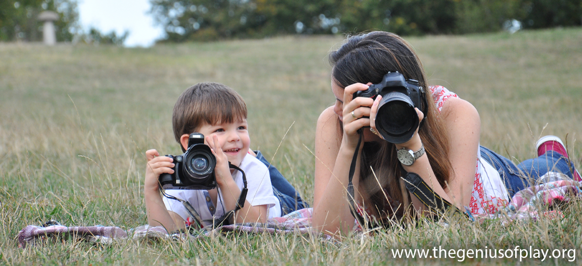 mom and young son laying in an open field taking pictures with a digital camera